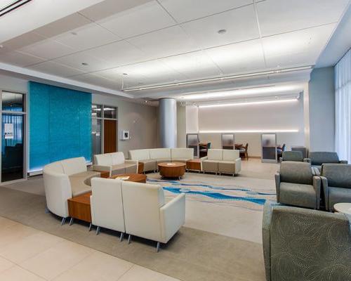 Interior photo of a waiting area. Cream colored chairs are in a U shape in the center of the room.